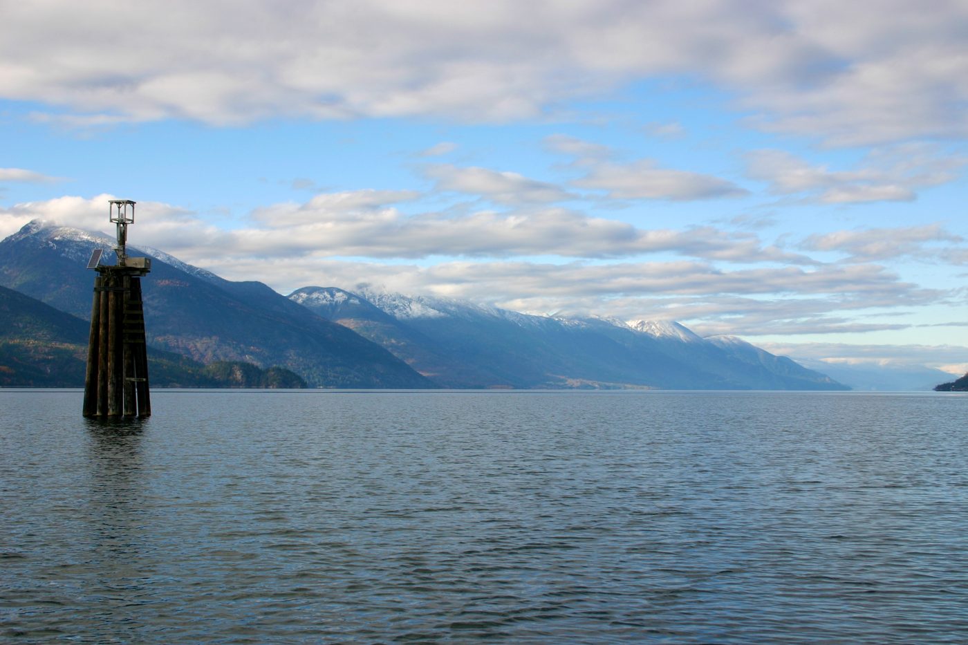 Kootenay Lake on a calm day, with a lighthouse marker and mountains in the distance